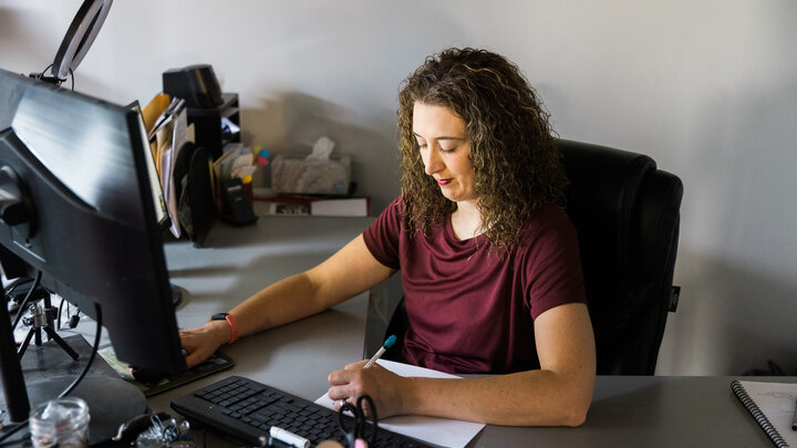 Woman working at a desk, typing on a keyboard, with papers and office supplies nearby.