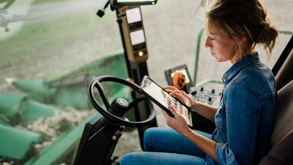 Female in cab of a combine using tablet.