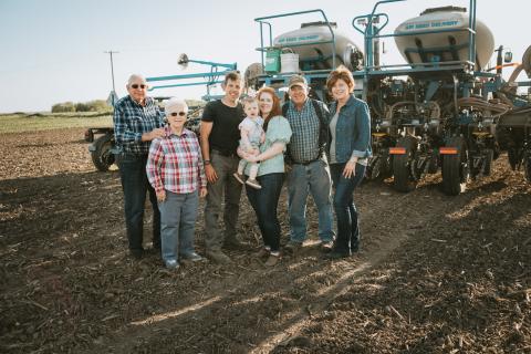 Multi-generational family posing in front of farm equipment.